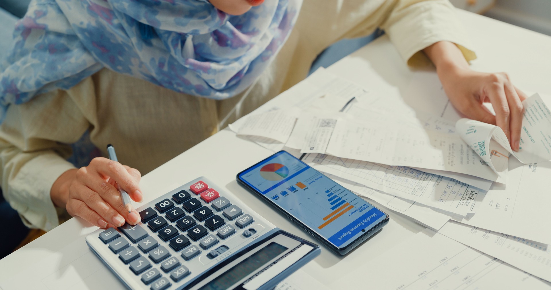 Close up Asian muslim woman with hijab using phone calculator focus on utility bills calculate check credit card receipt monthly expense bill in living room at house.